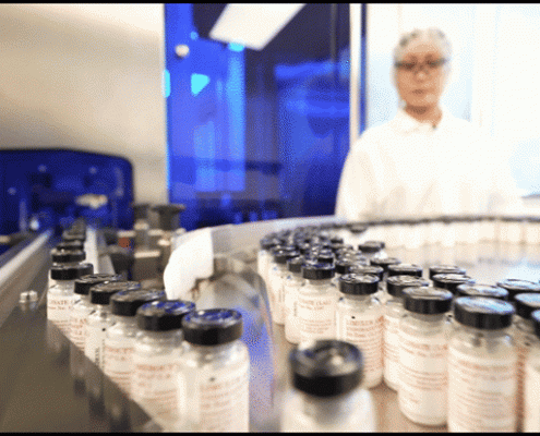 Vials moving along a pharmaceutical manufacturing line with technician in the background Vials moving along a pharmaceutical manufacturing line with technician in the background