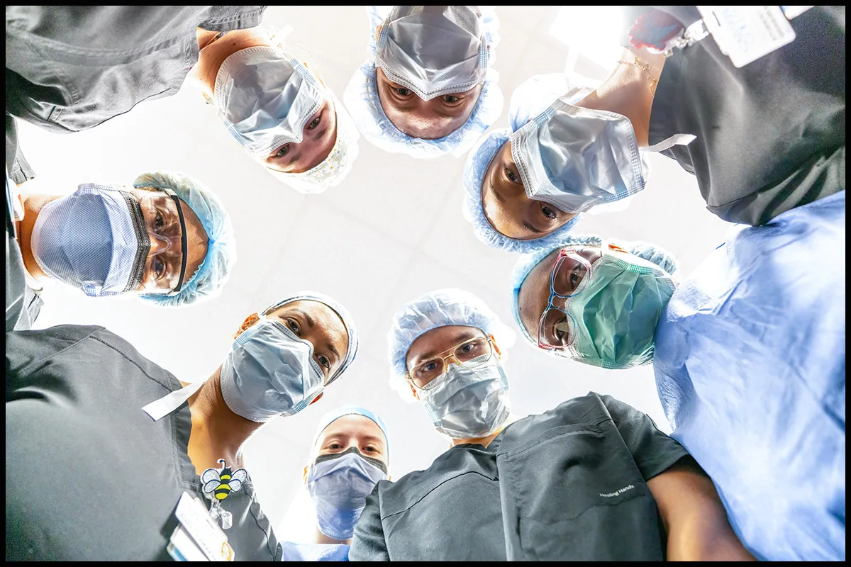 HOME 1 Surgical team wearing masks and caps viewed from the patient’s perspective in an operating room
