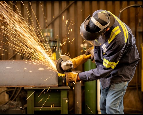 Grinding structural steel during fabrication operations. Industrial worker grinding a structural steel beam with sparks flying inside a fabrication shop