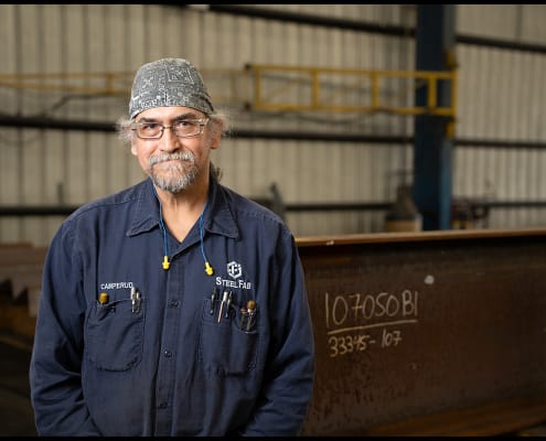Portrait captured inside a steel fabrication shop. Industrial worker standing in front of steel beams inside a fabrication facility