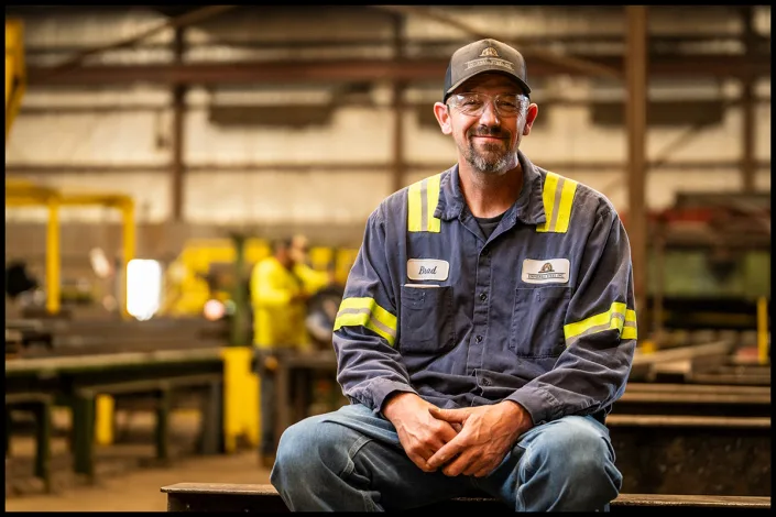 Environmental portrait of an industrial worker in a fabrication facility. Industrial worker seated inside a steel fabrication shop