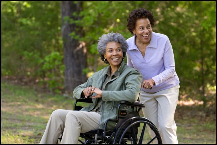Caregiver pushing senior in wheelchair along outdoor path