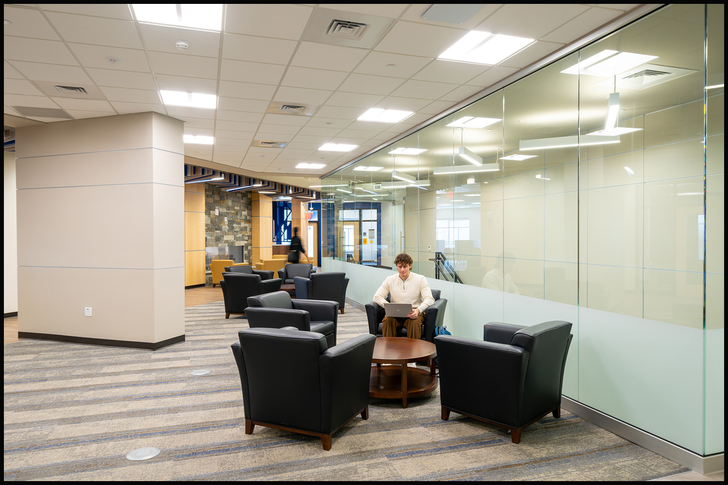 University interior photograph of a modern lobby with seating areas and a student working on a laptop.