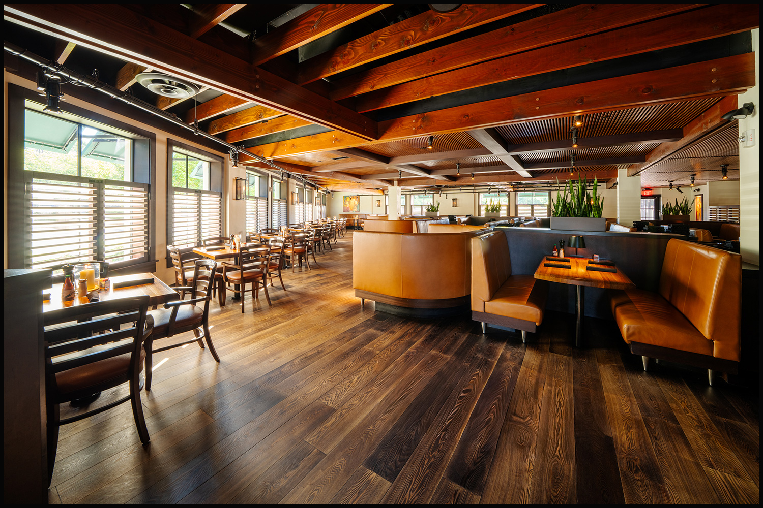 Commercial architectural photograph of an upscale restaurant dining room with booths, wood finishes, and natural light.