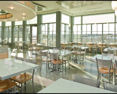 Bright waterfront dining interior with floor-to-ceiling windows and modern seating